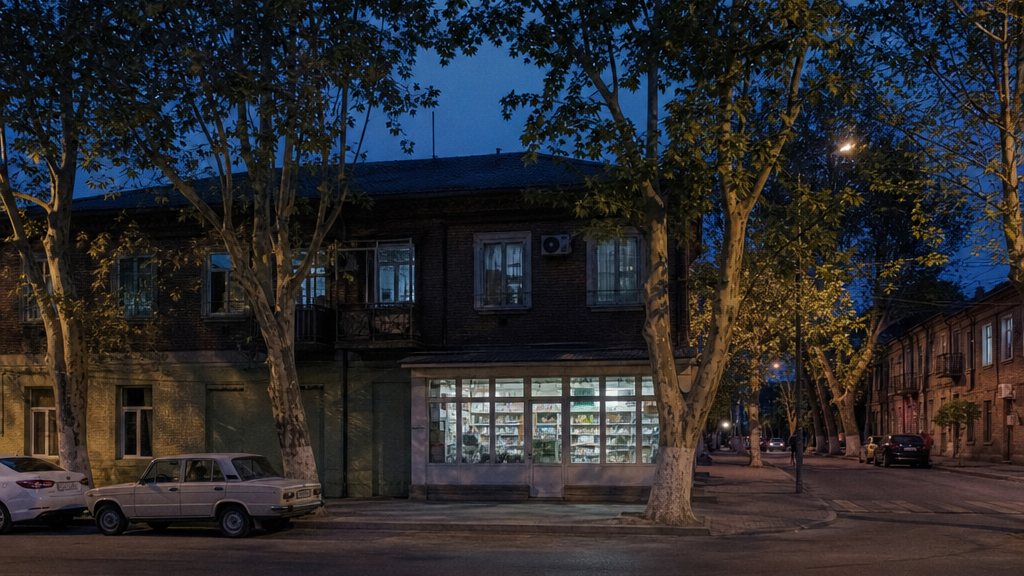Вечерняя улица Краснодара с освещённой витриной продуктового магазина на первом этаже